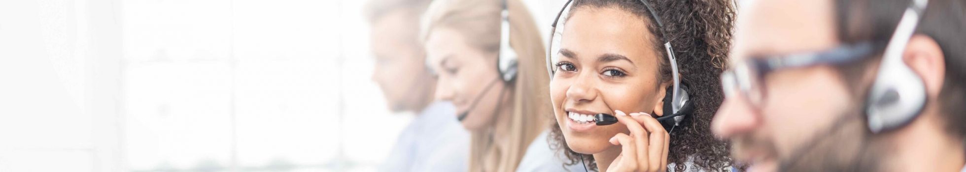 Call center worker accompanied by her team. Smiling customer support operator at work. Young employee working with a headset.